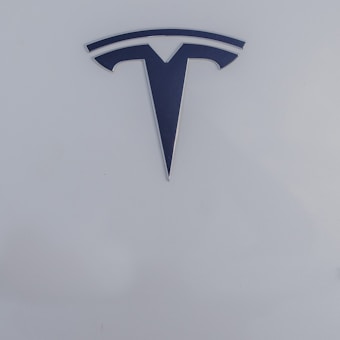 A sleek, metallic logo in the shape of a T sits prominently against a smooth, white background, conveying a sense of modern elegance and sophistication.